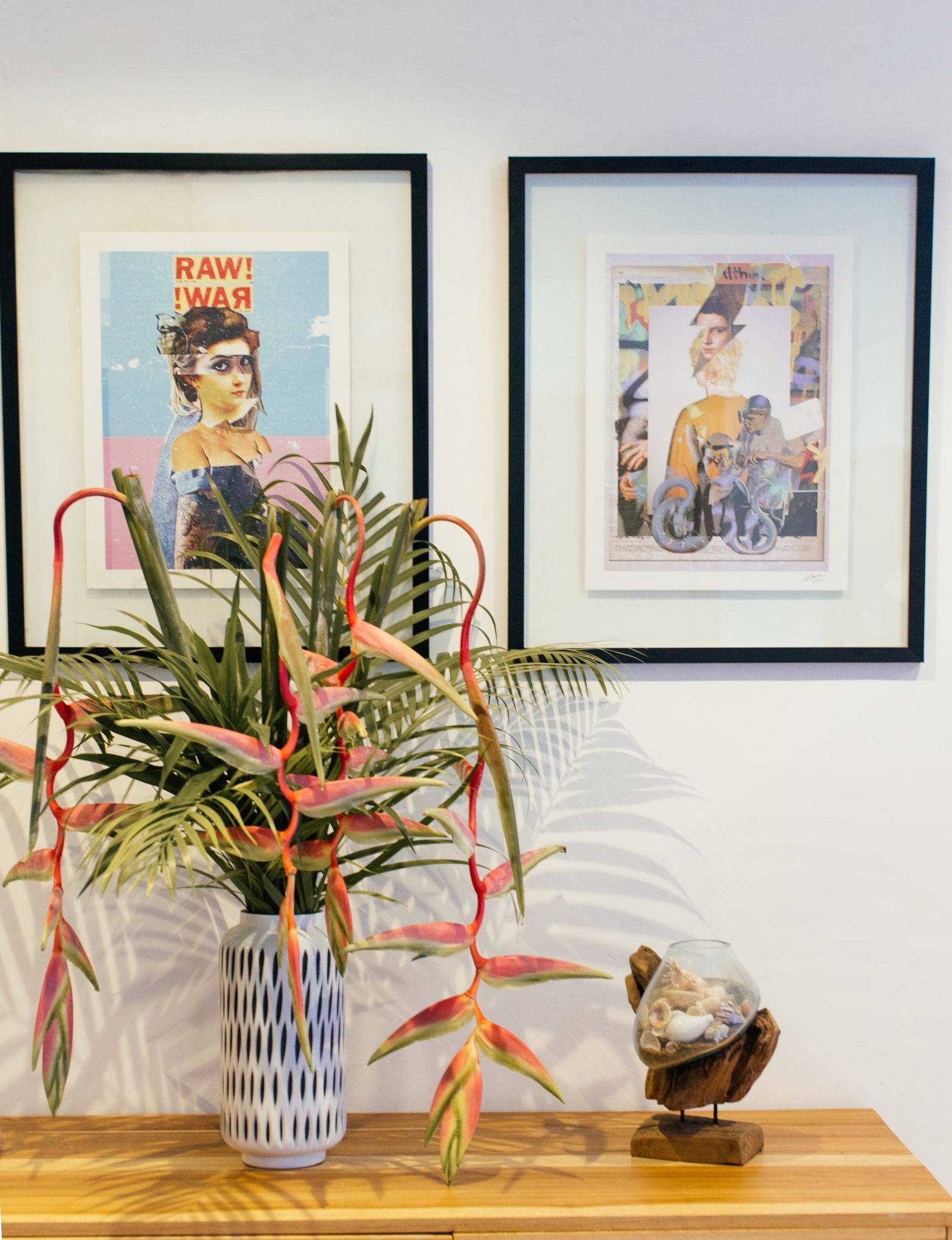 Two colorful framed collage prints above a wooden console with tropical flowers